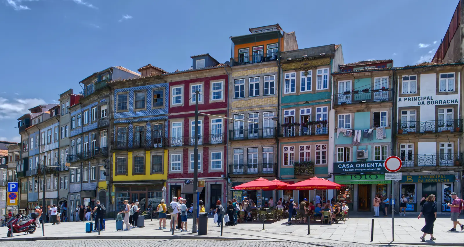 Colourful historic façades and café terraces lining a sunny square in central Porto.
